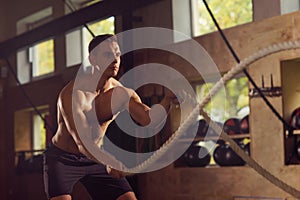 Fit, sporty and athletic sportsman working in a gym. Man training using battle ropes. Sports, athletics and fitness