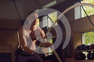 Fit, sporty and athletic sportsman working in a gym. Man training using battle ropes. Sports, athletics and fitness
