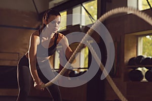 Fit, sporty and athletic sportswoman working in a gym. Woman training using battle ropes. Sports, athletics and fitness