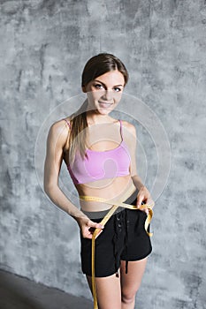 Fit and sporty girl measuring her perfect body on gray stylish background.