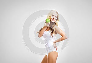 Fit and sporty girl in white underwear. Beautiful and healthy woman eating green apple over grey background. Sport, fitness, diet