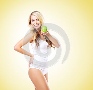 Fit and sporty girl in white underwear. Beautiful and healthy woman eating green apple over yellow background. Sport, fitness, di
