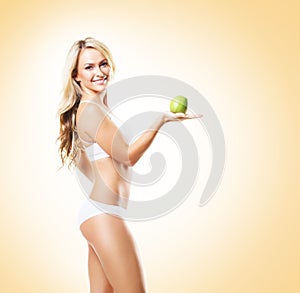 Fit and sporty girl in white underwear. Beautiful and healthy woman eating green apple over yellow background. Sport, fitness, di