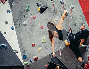 Fit sporty student girl moving up at rock climbing wall at the gym