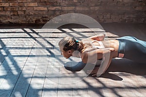 Fit sporty woman doing pushups in sunny gym on wooden floor, closeup.