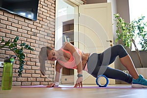 Fit sporty woman rolling on foam massage roller doing exercise at home.