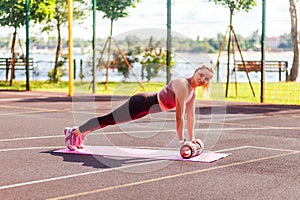 Fit sporty woman training on mat outdoor summer day, performing perfect plank with foam roller massager