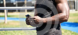 Fit sporty young black man using phone standing in workout park. Closeup