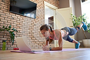 Fit sporty young woman doing online workout exercise watching video at home.