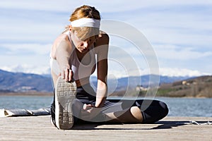 Fit and sporty young woman doing stretching next to the lake.