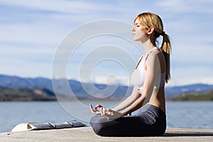 Fit and sporty young woman doing yoga next to the lake.