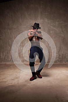 Fit strong physique African American young man wearing black hat and trousers posing dancing