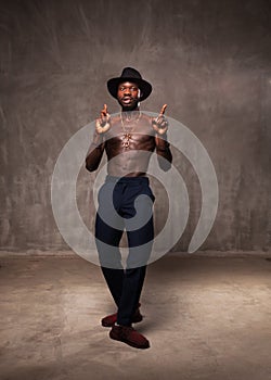 Fit strong physique African American young man wearing black hat and trousers posing dancing