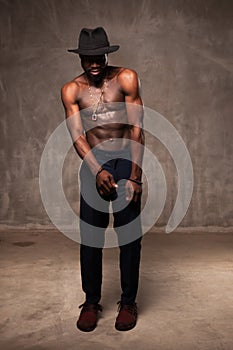 Fit strong physique African American young man wearing black hat and trousers posing dancing