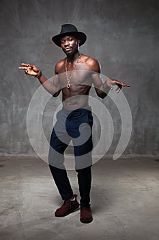 Fit strong physique African American young man wearing black hat and trousers posing dancing