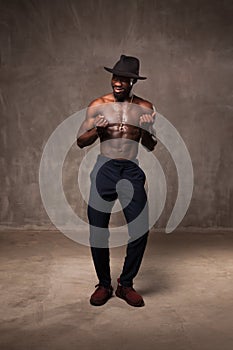 Fit strong physique African American young man wearing black hat and trousers posing dancing