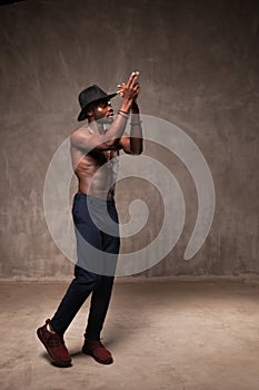 Fit strong physique African American young man wearing black hat and trousers posing dancing