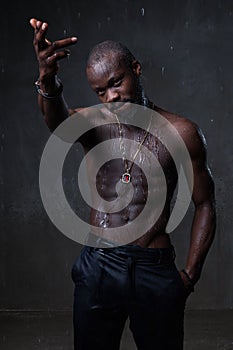 Fit strong physique African American young man wearing black hat and trousers posing dancing