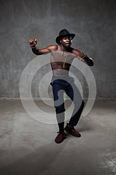 Fit strong physique African American young man wearing black hat and trousers posing dancing