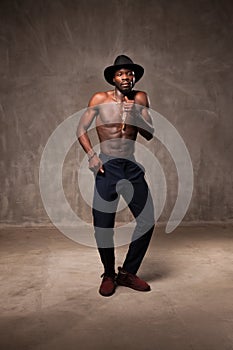 Fit strong physique African American young man wearing black hat and trousers posing dancing