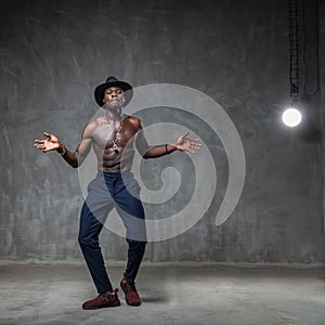 Fit strong physique African American young man wearing black hat and trousers posing dancing