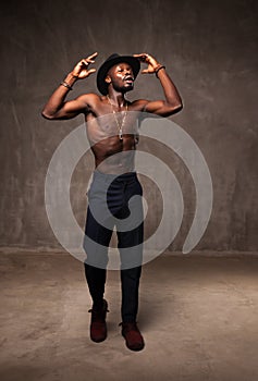 Fit strong physique African American young man wearing black hat and trousers posing dancing