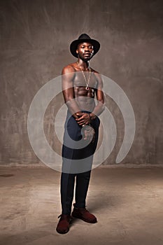 Fit strong physique African American young man wearing black hat and trousers posing dancing