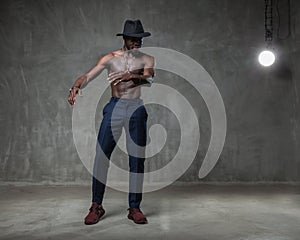 Fit strong physique African American young man wearing black hat and trousers posing dancing