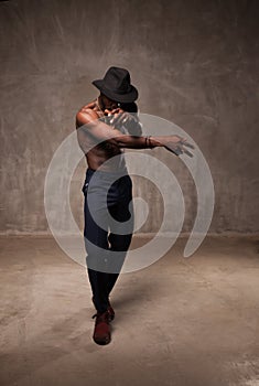 Fit strong physique African American young man wearing black hat and trousers posing dancing