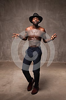 Fit strong physique African American young man wearing black hat and trousers posing dancing