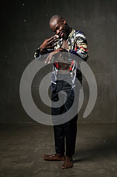 Fit strong physique African American young man wearing black hat and trousers posing dancing