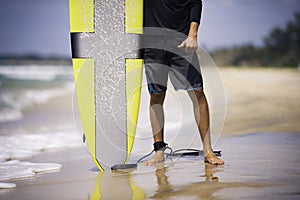 Surfer holds surfboard on the sunny beach showing shaka. Summer holiday hobby