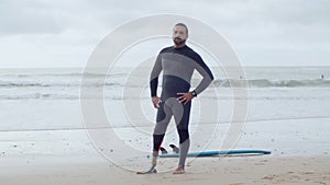 Fit surfer in wetsuit with bionic leg standing on ocean beach