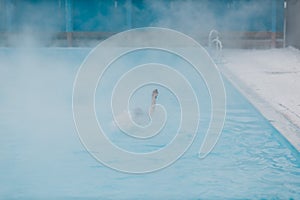 Fit swimmer male training swim in open winter swimming pool with fog. Geothermal outdoor spa concept.