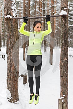 Fit woman athlete performing pull ups in a bar. Winter street outdoor training workout.