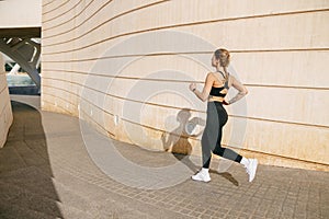 Fit woman athlete in sportswear is running on modern buildings background. Active lifestyle concept