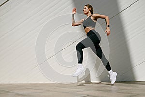 Fit woman athlete in sportswear is running on modern buildings background. Active lifestyle concept