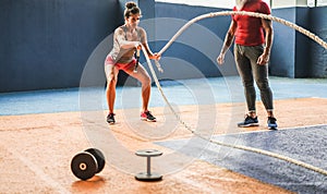 Fit woman with battle rope in functional training fitness gym - Personal trainer motivating female athlete inside wellness club