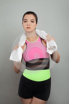 Fit woman brunette female model in sportsuit holding white towel after workout against gray studio wall background