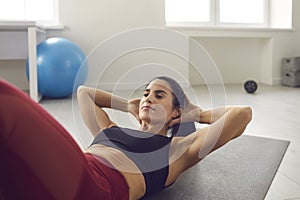 Fit woman doing crunches or sit-ups on gym mat during routine sports workout at home
