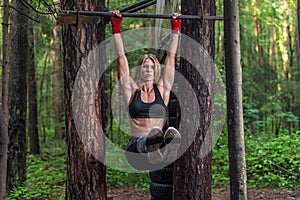 Fit woman doing hanging leg lifts abs muscles exercise on horisontal bar working out outside