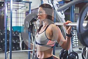 Fit woman doing squat with barbell in the gym.