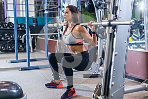 Fit woman doing squats with a barbell in Smith machine.