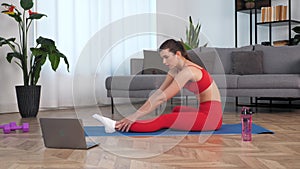 Fit woman doing warm-up stretching exercise on yoga or fitness blue mat at home