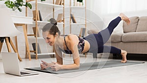 Fit woman doing yoga plank and watching online tutorials on laptop