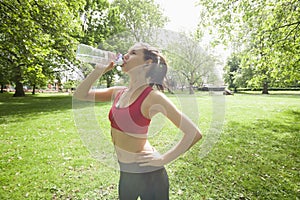 Fit woman drinking water while listening to music in park