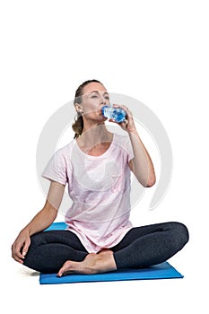 Fit woman drinking water while sitting on mat