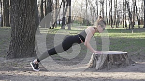 Fit woman exercising in woods doing push ups on a log at park. Exercising in open air natural gym. Push ups. Attractive