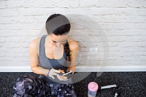 Fit woman in gym holding smart phone, brick wall