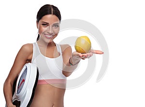 Fit woman holding a scale offers you an apple